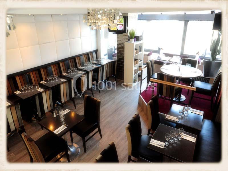 Salle de restaurant lumineuse avec tables dressées, chaises colorées et grandes fenêtres laissant entrer la lumière…