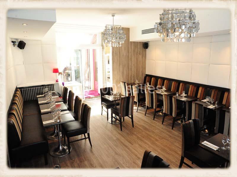 Salle de restaurant lumineuse avec tables alignées, chaises rembourrées et lustres modernes.