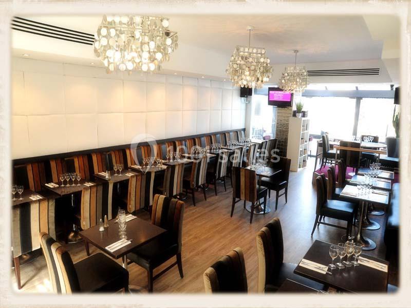 Salle de restaurant lumineuse avec tables dressées, chaises colorées et lustres modernes suspendus au plafond.