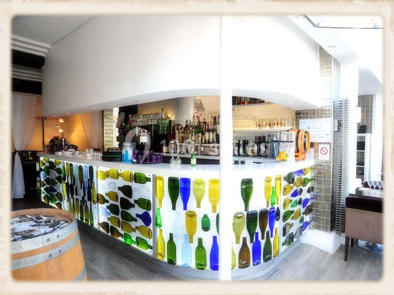 Bar lumineux avec comptoir décoré de bouteilles colorées, entouré de tabourets et éclairé par une lumière douce.