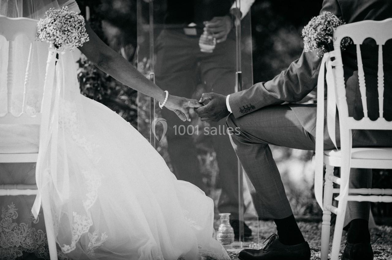 Un couple assis se tenant la main lors d'une cérémonie de mariage en extérieur, capturé en noir et blanc.