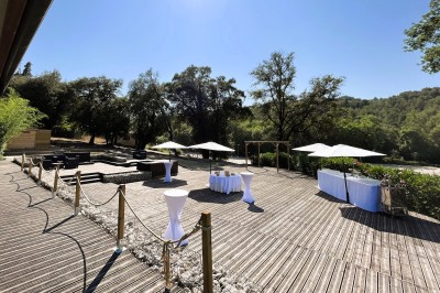 Miniature Location salle Villeneuve-Loubet (Alpes-Maritimes) - Carré des Cavaliers #7 Terrasse en bois aménagée avec tables hautes, parasols et mobilier, entourée de végétation sous un ciel dégagé.