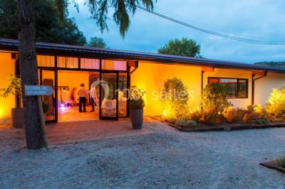 Entrée d'un bâtiment éclairé en soirée, avec des plantes décoratives et des personnes visibles à l'intérieur.