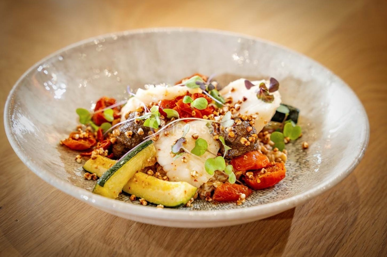 Assiette de légumes grillés avec courgettes, tomates cerises, herbes fraîches et céréales, présentée sur une table en bois.