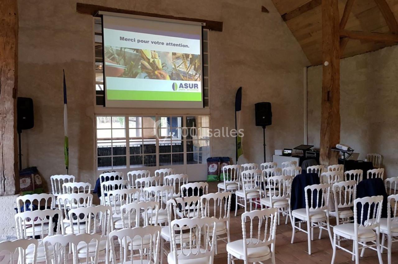 Salle de conférence avec des chaises blanches alignées, un écran de projection allumé et des équipements audio.