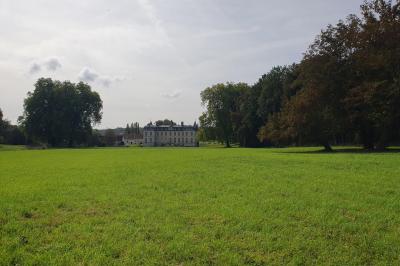 Serre éclairée au crépuscule, entourée de bâtiments anciens et d'arbres, avec un étang au premier plan.