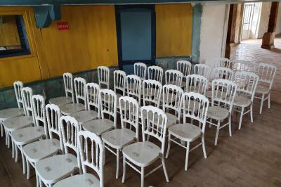 Serre éclairée au crépuscule, entourée de bâtiments anciens et d'arbres, avec un étang au premier plan.