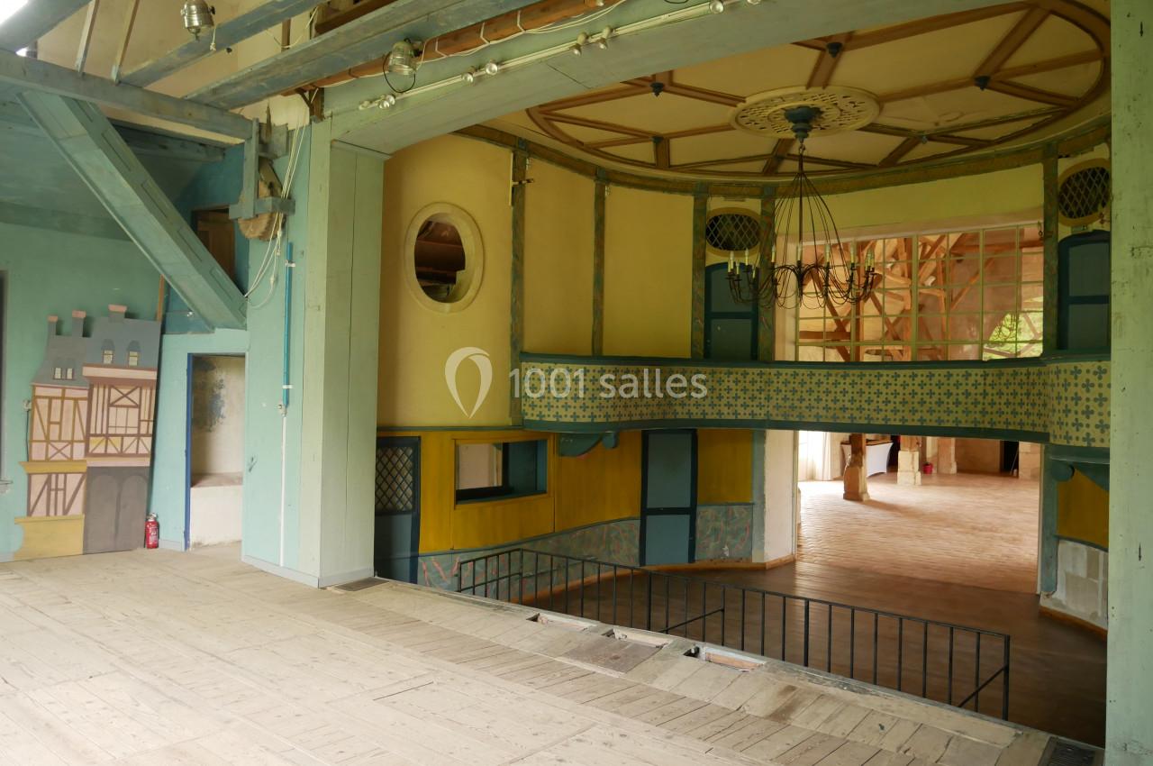 Intérieur d'un théâtre ancien avec scène en bois, balcons décorés et plafond orné d'un lustre.