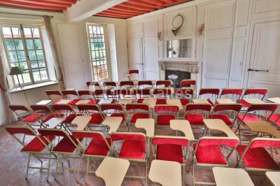 Serre éclairée au crépuscule, entourée de bâtiments anciens et d'arbres, avec un étang au premier plan.