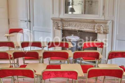 Serre éclairée au crépuscule, entourée de bâtiments anciens et d'arbres, avec un étang au premier plan.