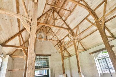 Serre éclairée au crépuscule, entourée de bâtiments anciens et d'arbres, avec un étang au premier plan.