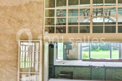 Serre éclairée au crépuscule, entourée de bâtiments anciens et d'arbres, avec un étang au premier plan.