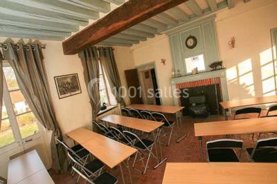 Serre éclairée au crépuscule, entourée de bâtiments anciens et d'arbres, avec un étang au premier plan.