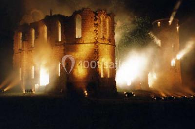 Salle de réception décorée avec des tables rondes, nappes blanches, chandeliers et guirlandes florales suspendues.