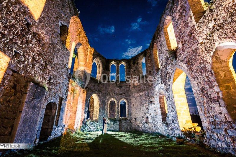 Ruines d'un édifice illuminées la nuit, avec une personne debout au centre sous un ciel étoilé.