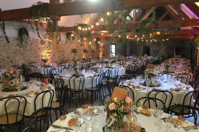 Salle de réception décorée avec des tables rondes, nappes blanches, chandeliers et guirlandes florales suspendues.