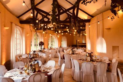 Salle de réception décorée avec des tables rondes, nappes blanches, chandeliers et guirlandes florales suspendues.