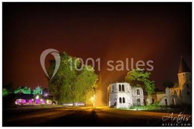 Salle de réception décorée avec des tables rondes, nappes blanches, chandeliers et guirlandes florales suspendues.