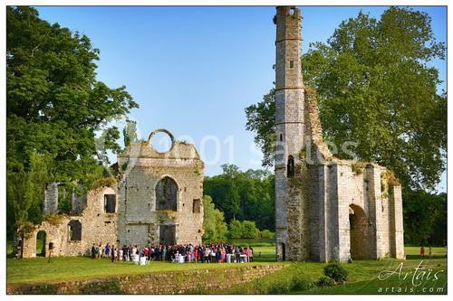 Ruines d'une ancienne abbaye entourées de verdure, avec un groupe de personnes rassemblées devant.