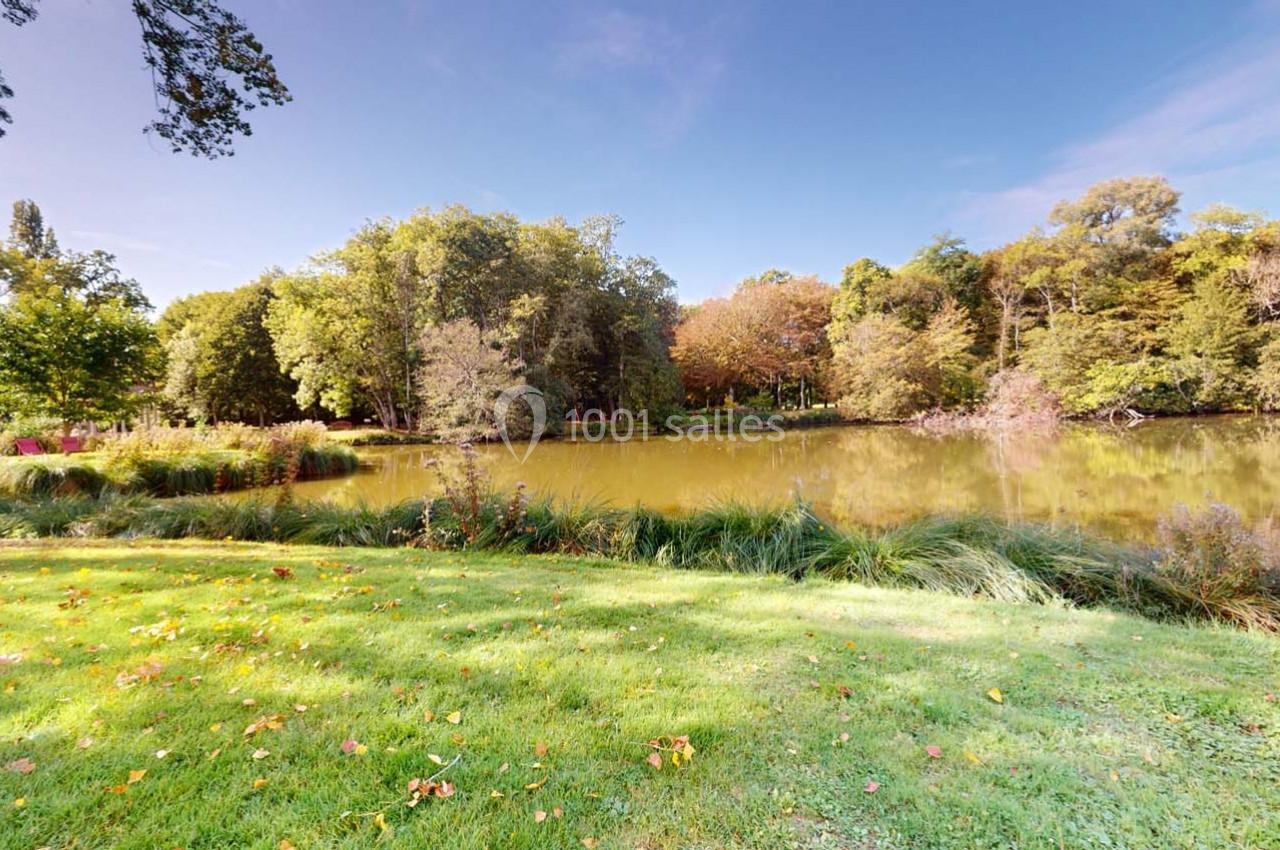 Vue d'un étang entouré d'arbres et de pelouses verdoyantes sous un ciel dégagé.