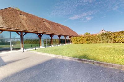 Espace d'attente avec fauteuils noirs, tables basses, escalier en bois courbé et plantes dans un intérieur lumineux.