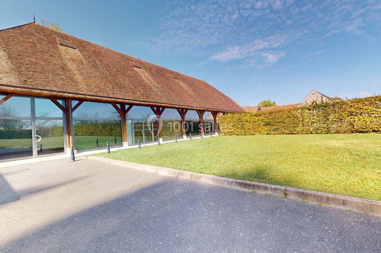 Bâtiment moderne avec façade en verre et toit en pente, entouré de pelouse et haies, sous un ciel dégagé.