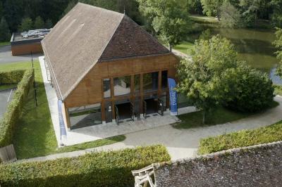 Espace d'attente avec fauteuils noirs, tables basses, escalier en bois courbé et plantes dans un intérieur lumineux.
