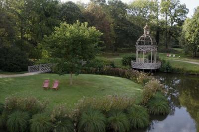 Espace d'attente avec fauteuils noirs, tables basses, escalier en bois courbé et plantes dans un intérieur lumineux.