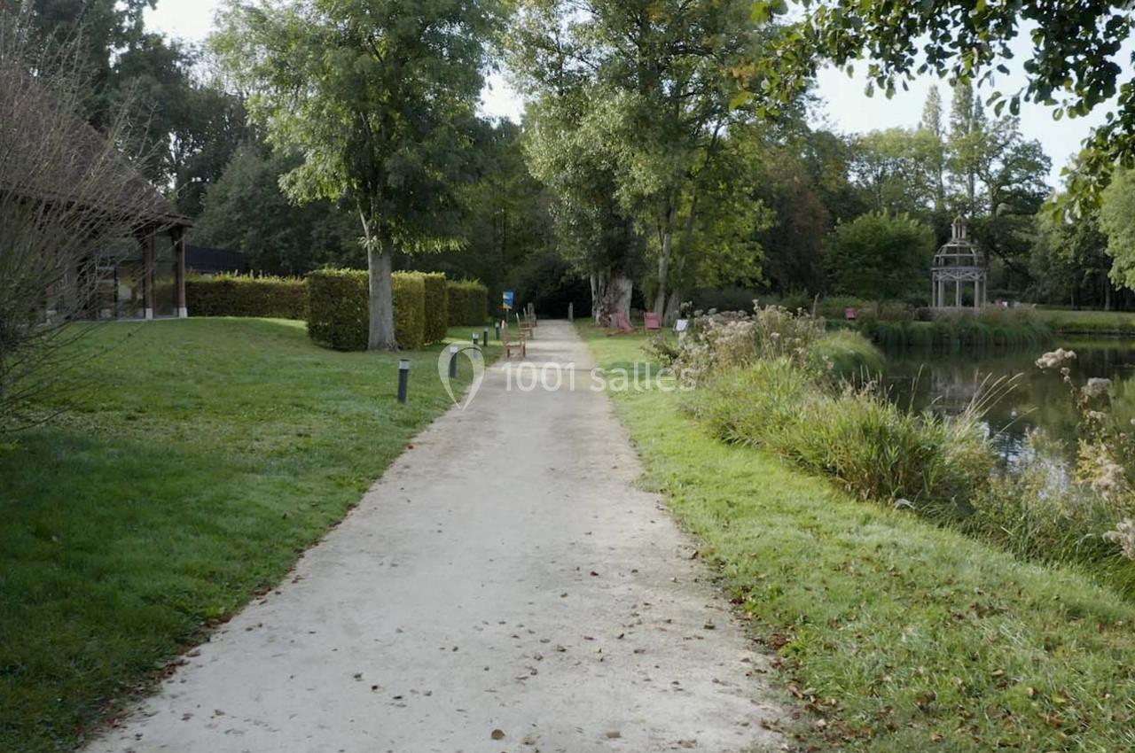Chemin de gravier bordé de verdure, longeant un étang et des arbres dans un parc calme.