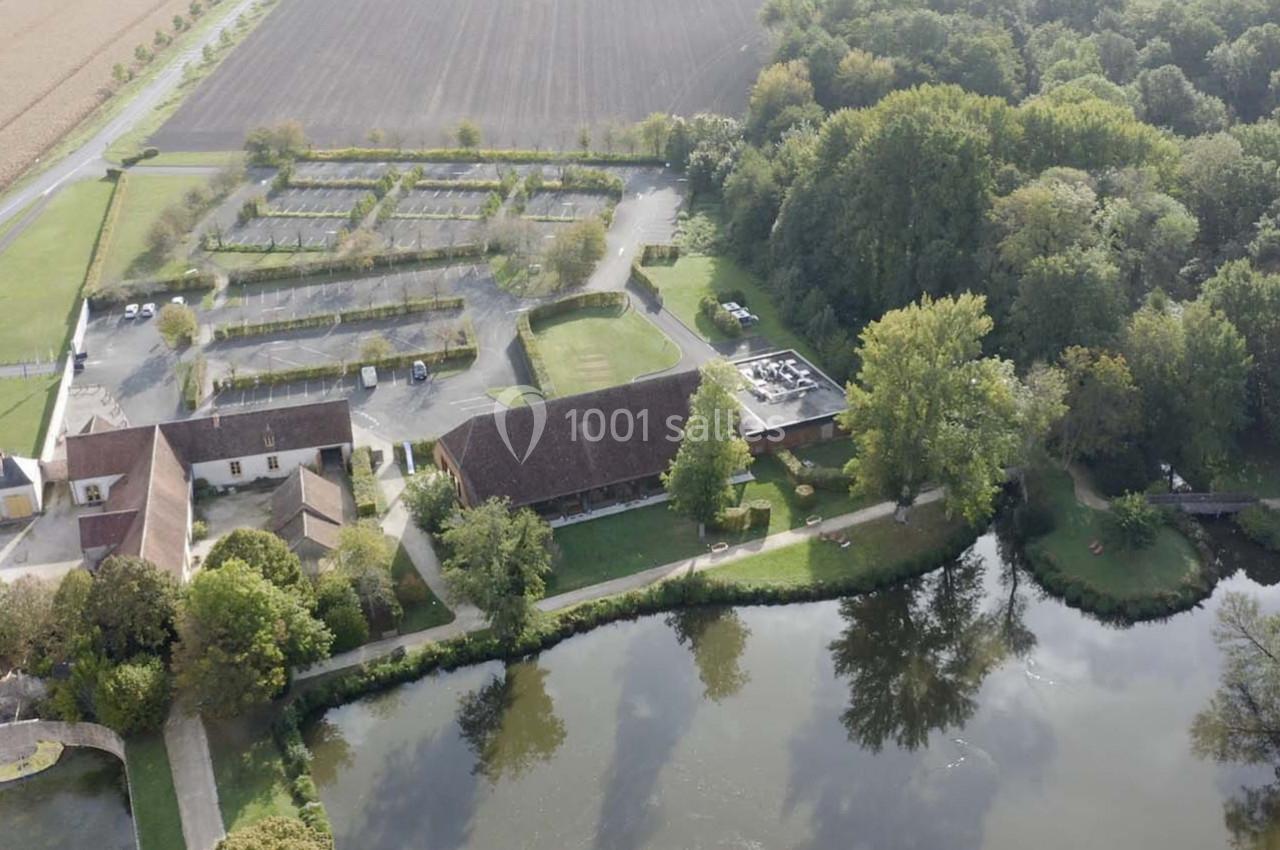 Vue aérienne d'un domaine rural avec bâtiments, parking, étang et forêt environnante.
