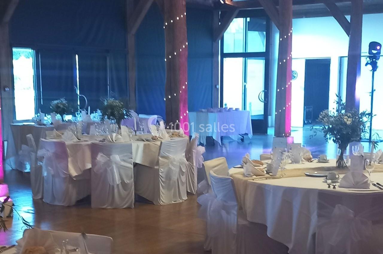 Salle de réception décorée avec des tables rondes, nappes blanches, chaises houssées et centres de table fleuris.