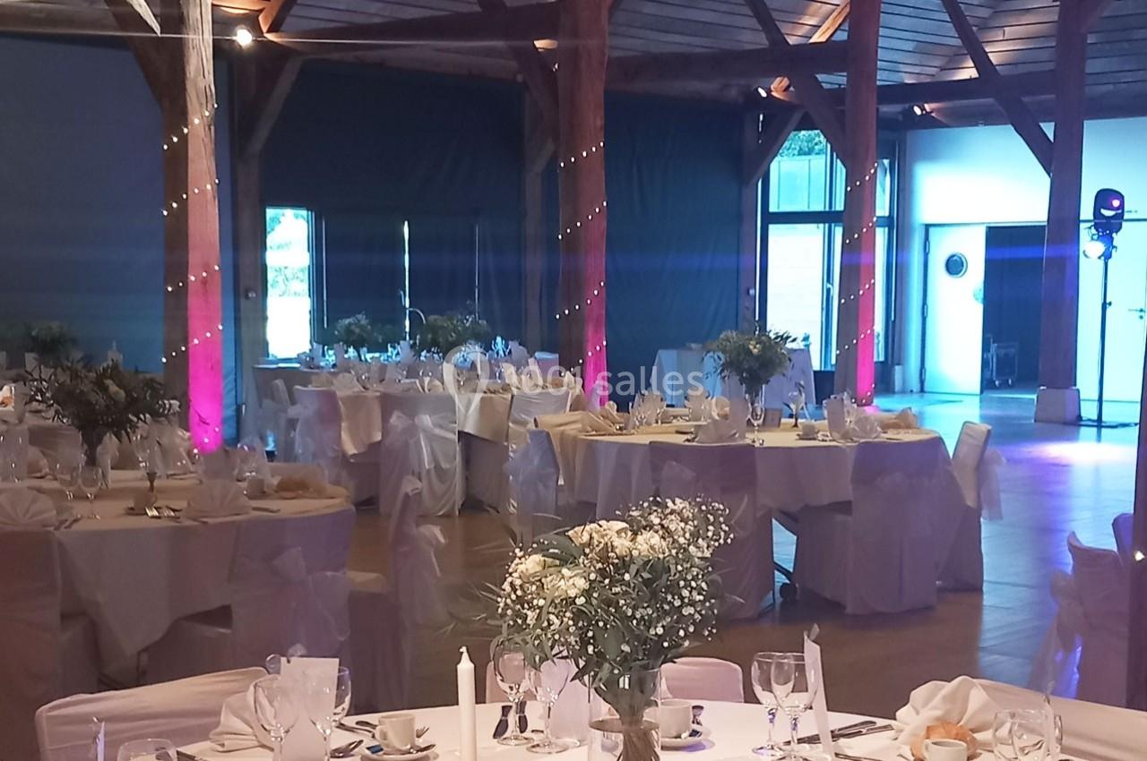 Salle de réception décorée pour un événement, avec tables dressées, nappes blanches et éclairage tamisé.