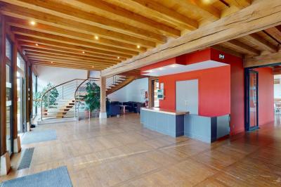 Espace d'attente avec fauteuils noirs, tables basses, escalier en bois courbé et plantes dans un intérieur lumineux.