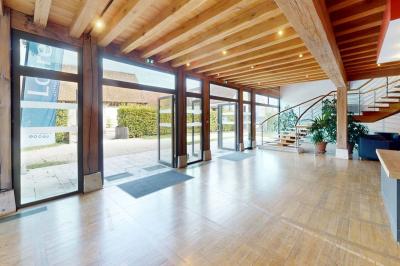 Espace d'attente avec fauteuils noirs, tables basses, escalier en bois courbé et plantes dans un intérieur lumineux.