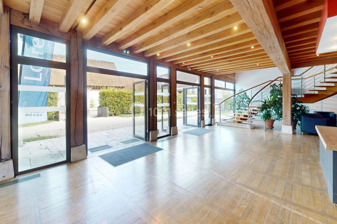 Intérieur lumineux avec parquet, poutres apparentes, escalier en bois et grandes baies vitrées donnant sur l'extérieur.