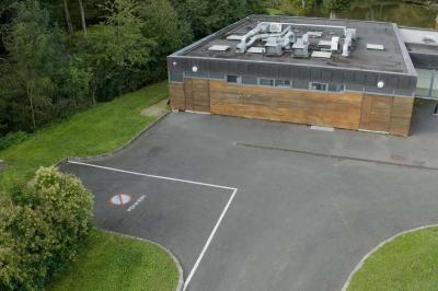 Espace d'attente avec fauteuils noirs, tables basses, escalier en bois courbé et plantes dans un intérieur lumineux.