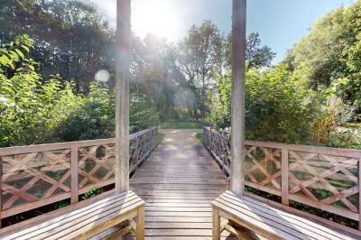 Espace d'attente avec fauteuils noirs, tables basses, escalier en bois courbé et plantes dans un intérieur lumineux.