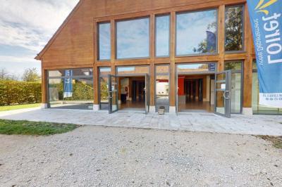 Espace d'attente avec fauteuils noirs, tables basses, escalier en bois courbé et plantes dans un intérieur lumineux.