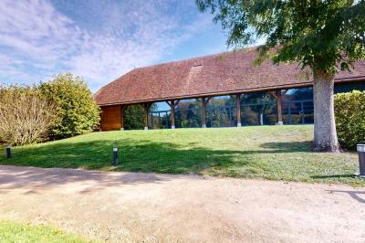 Espace d'attente avec fauteuils noirs, tables basses, escalier en bois courbé et plantes dans un intérieur lumineux.