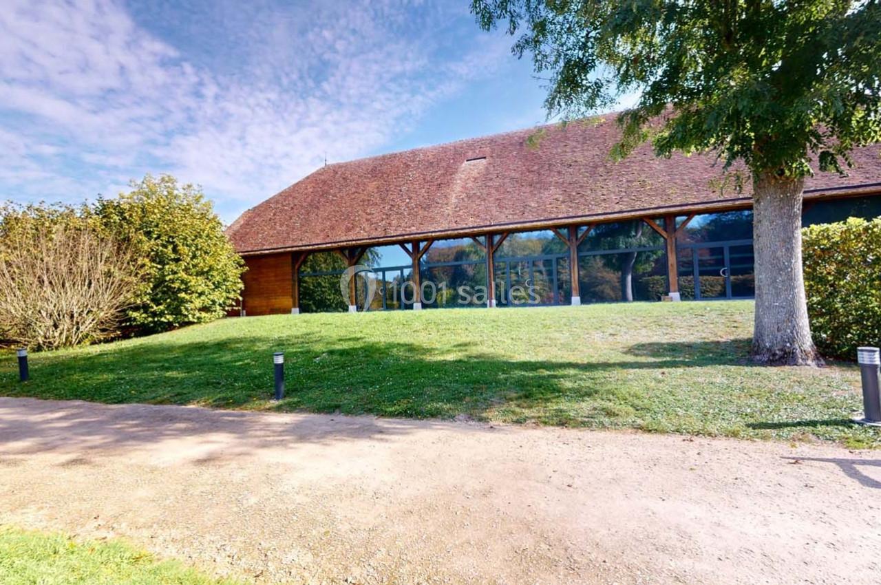 Bâtiment à toit en tuiles entouré de verdure, avec une façade vitrée et un chemin en premier plan.