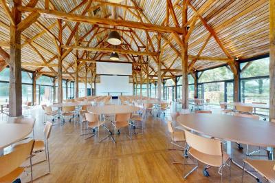 Espace d'attente avec fauteuils noirs, tables basses, escalier en bois courbé et plantes dans un intérieur lumineux.