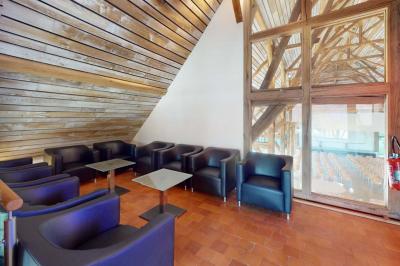 Espace d'attente avec fauteuils noirs, tables basses, escalier en bois courbé et plantes dans un intérieur lumineux.