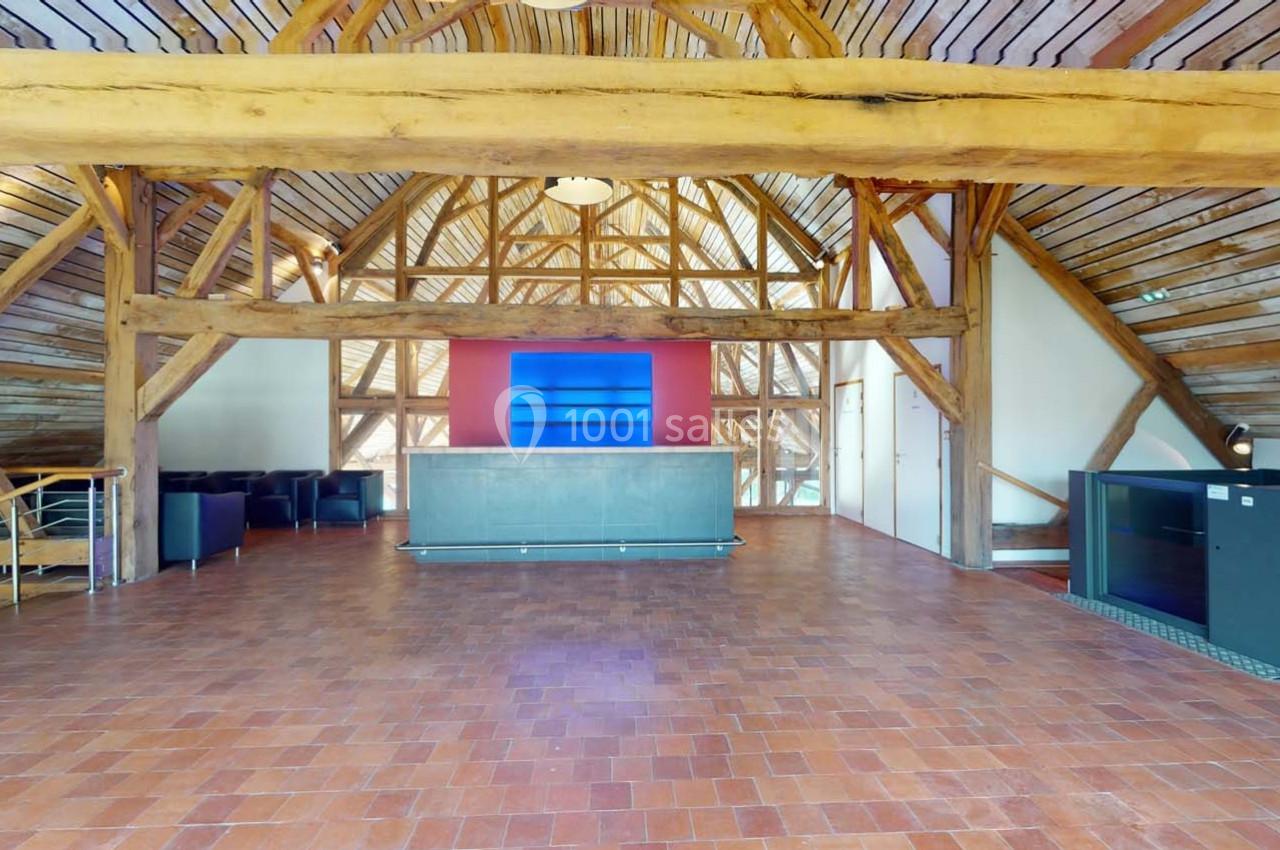 Salle spacieuse avec charpente en bois apparente, sol en carreaux rouges et comptoir central devant un mur coloré.