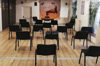 Salle de réunion lumineuse avec une grande table rectangulaire, des chaises noires et des fenêtres donnant sur l'extérieur.