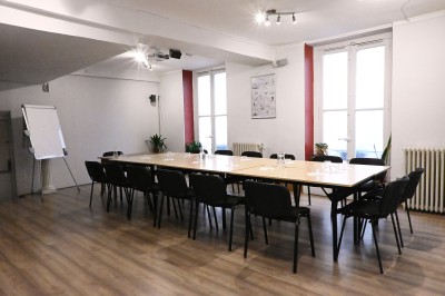 Salle de réunion lumineuse avec une grande table rectangulaire, des chaises noires et des fenêtres donnant sur l'extérieur.