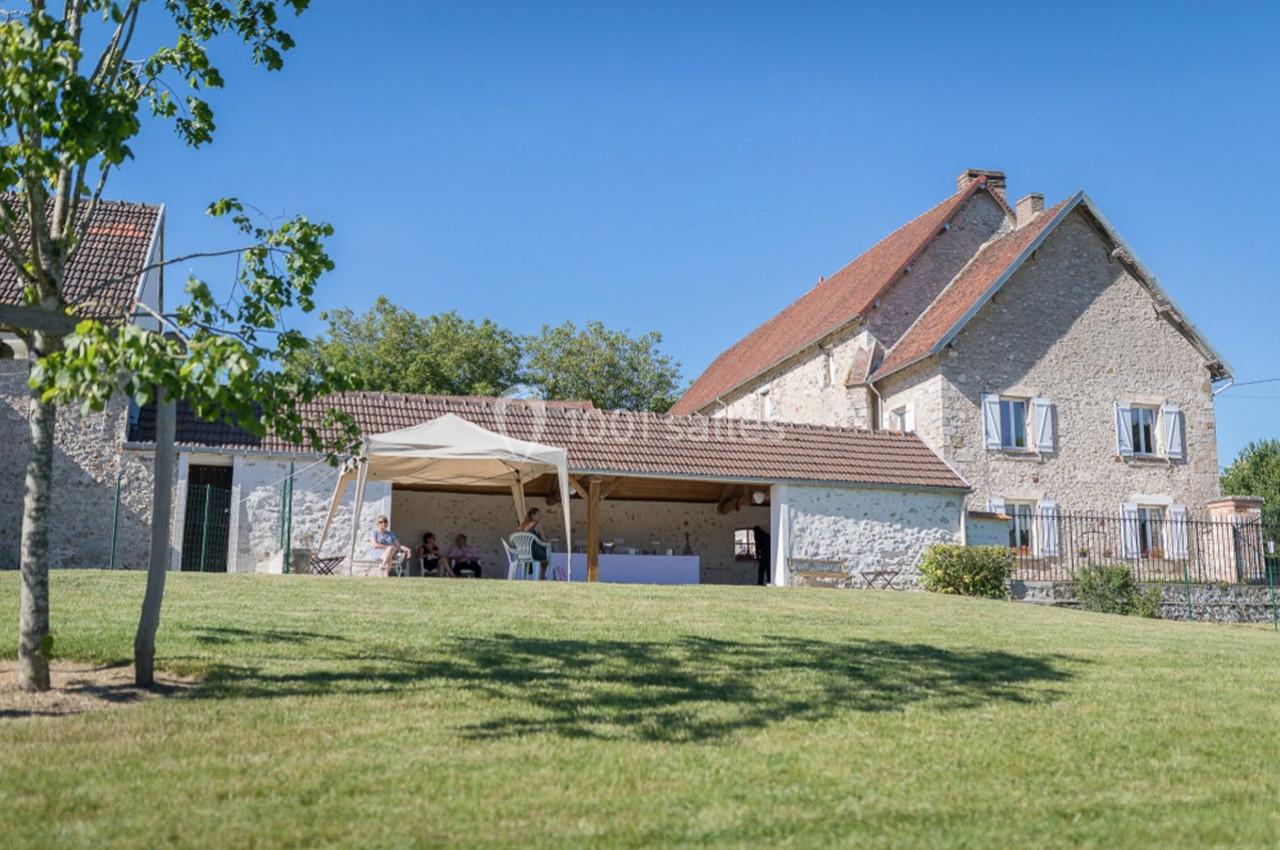 Maison en pierre avec toit en tuiles, jardin verdoyant et tonnelle blanche installée sur la pelouse.