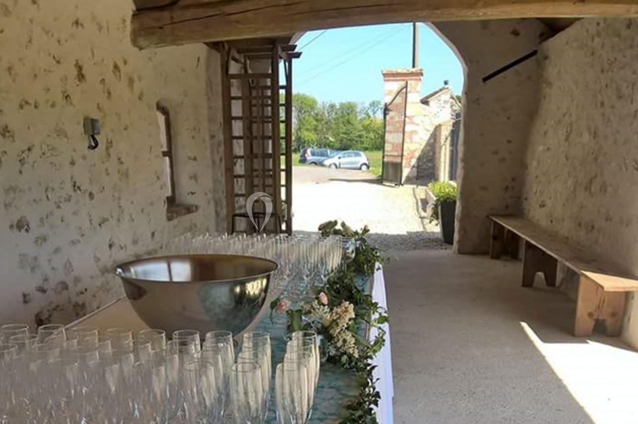 Table décorée avec des verres et une coupe en métal dans une grange ouverte, avec vue sur l'extérieur ensoleillé.