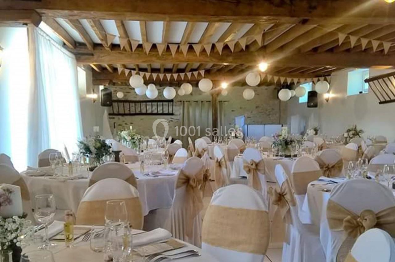 Salle de réception décorée avec des tables rondes, nappes blanches, chaises ornées de nœuds en toile de jute et guirlandes…