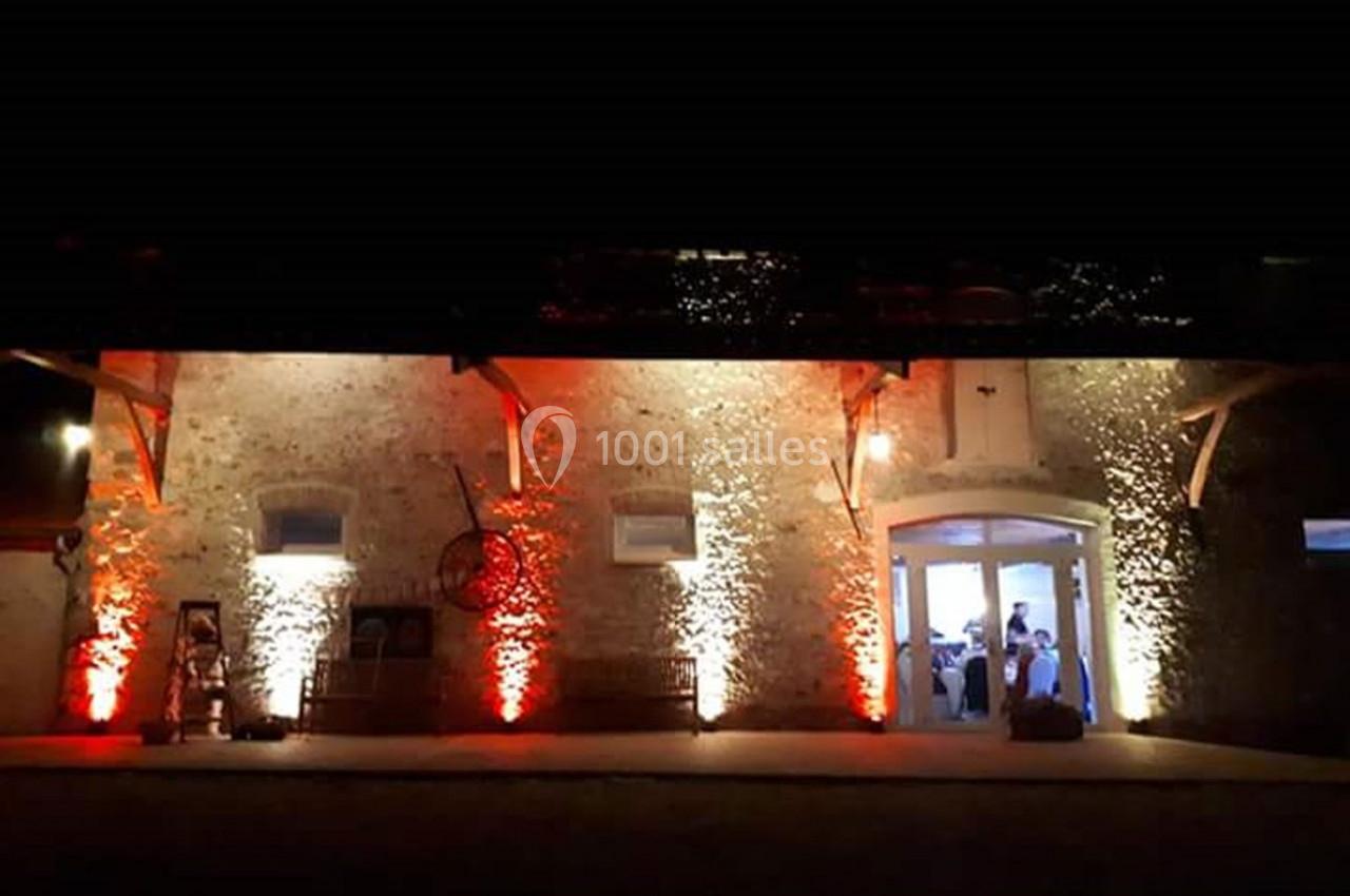 Façade en pierre éclairée par des lumières rouges et blanches, avec une porte ouverte laissant entrevoir un événement…