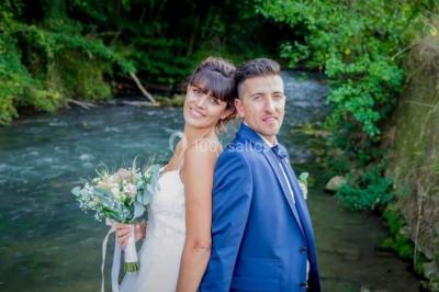 Un couple en tenue de mariage pose sur des rails entourés de verdure dans un cadre naturel et lumineux.